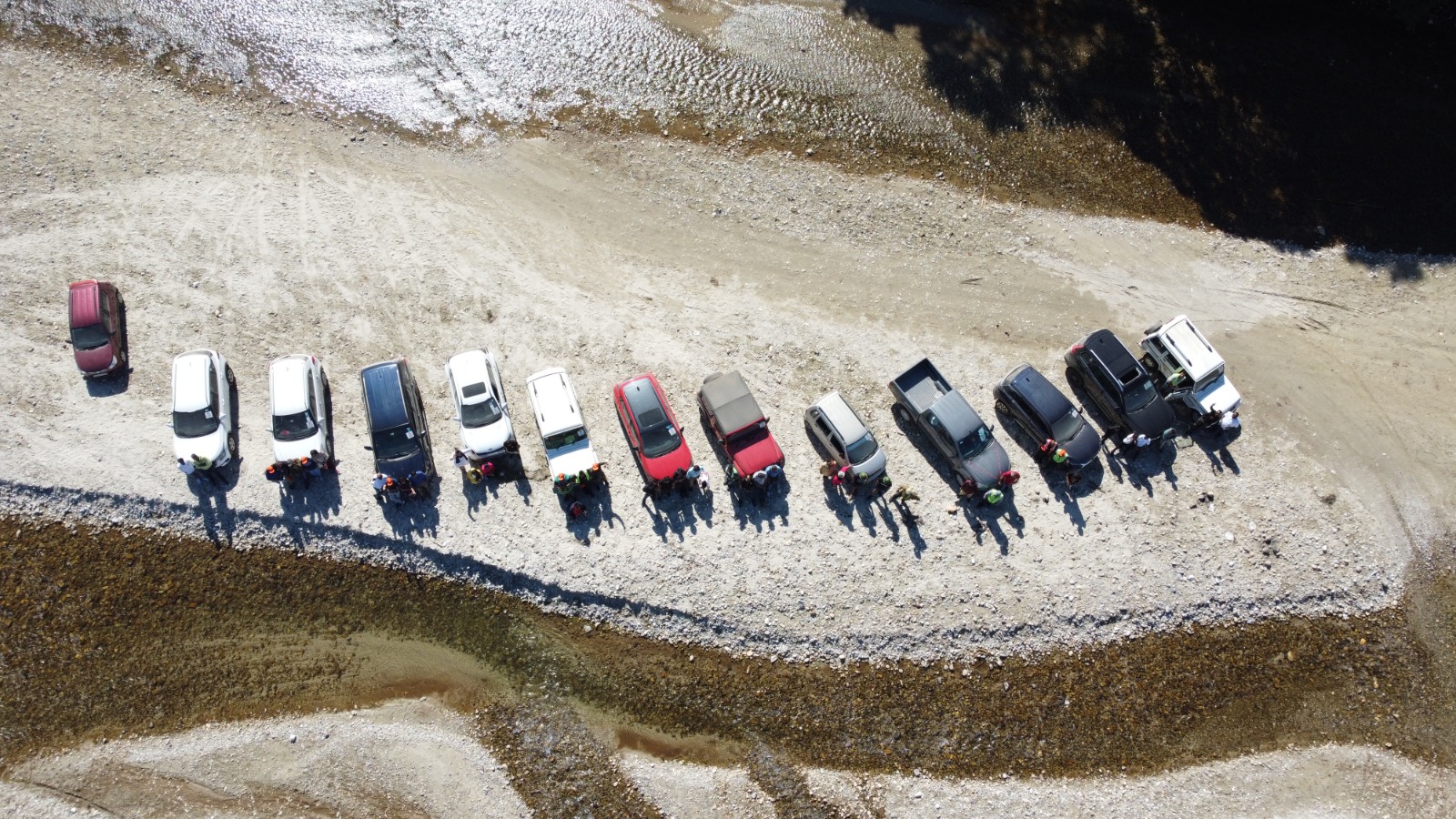 A convoy of vehicles gathered on a dry riverbed at the foothills